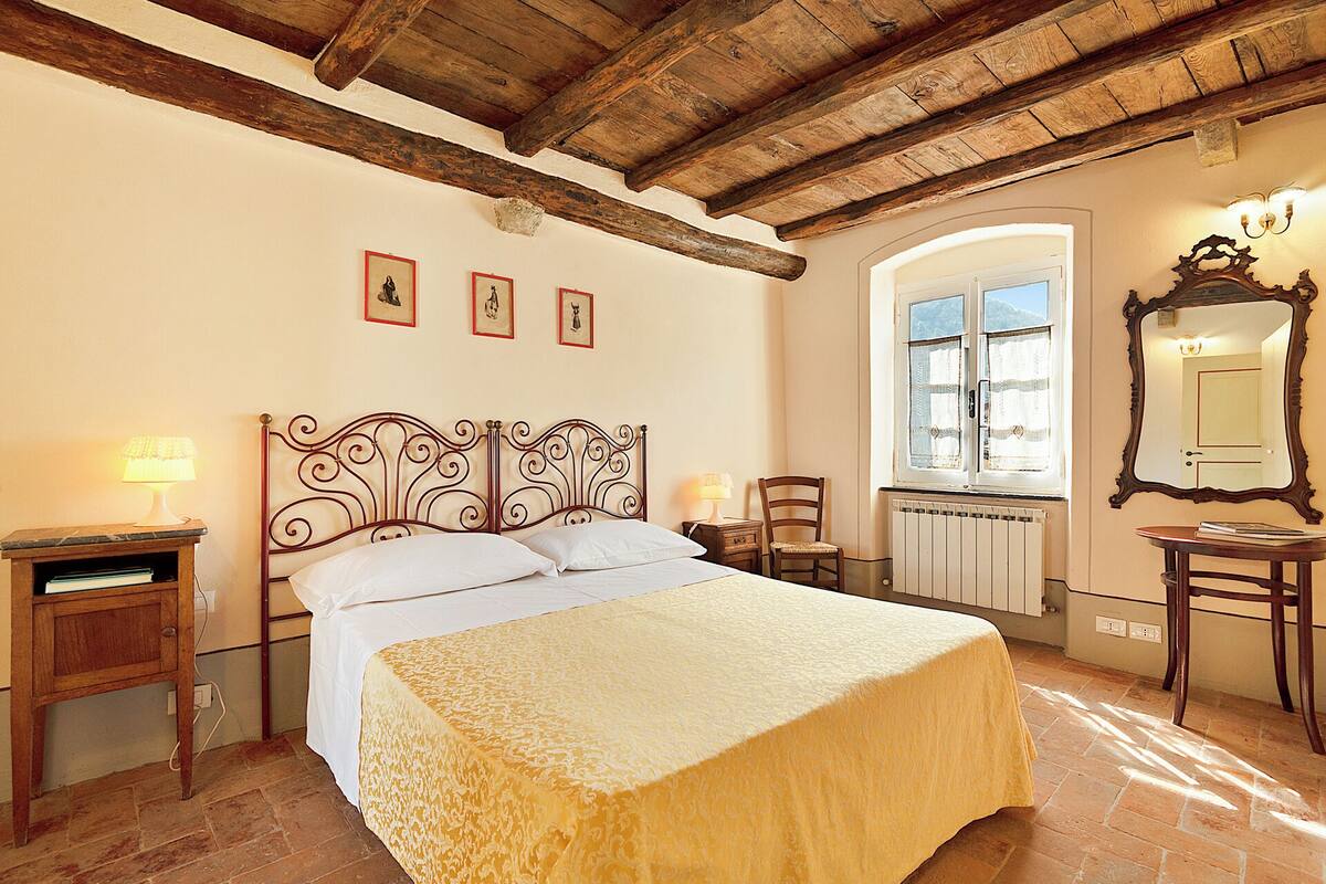 Un dormitorio con cama, dos mesitas de noche, una silla, ventana y espejo.