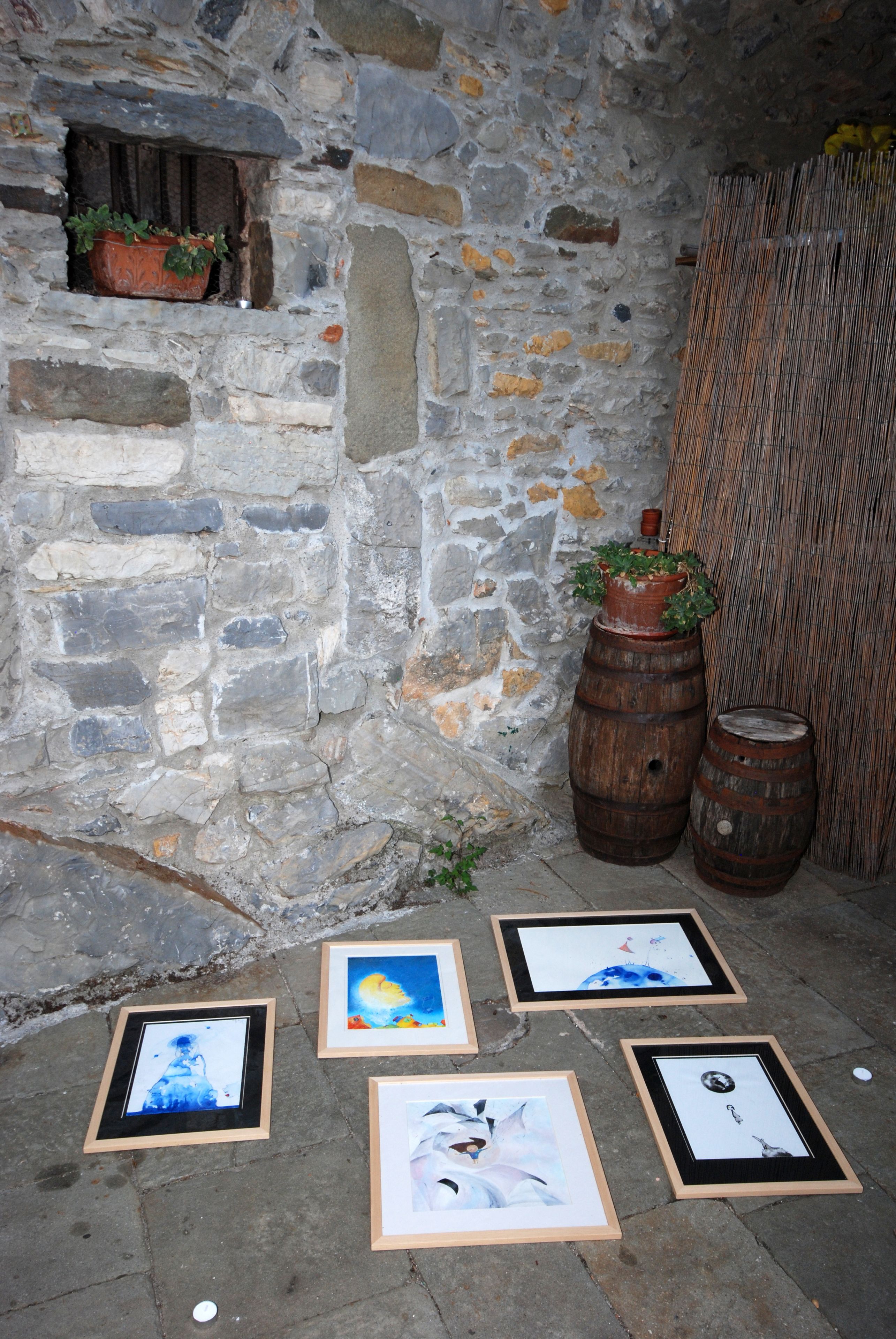A stone wall with a small window, wooden barrels, and framed artworks on the ground.