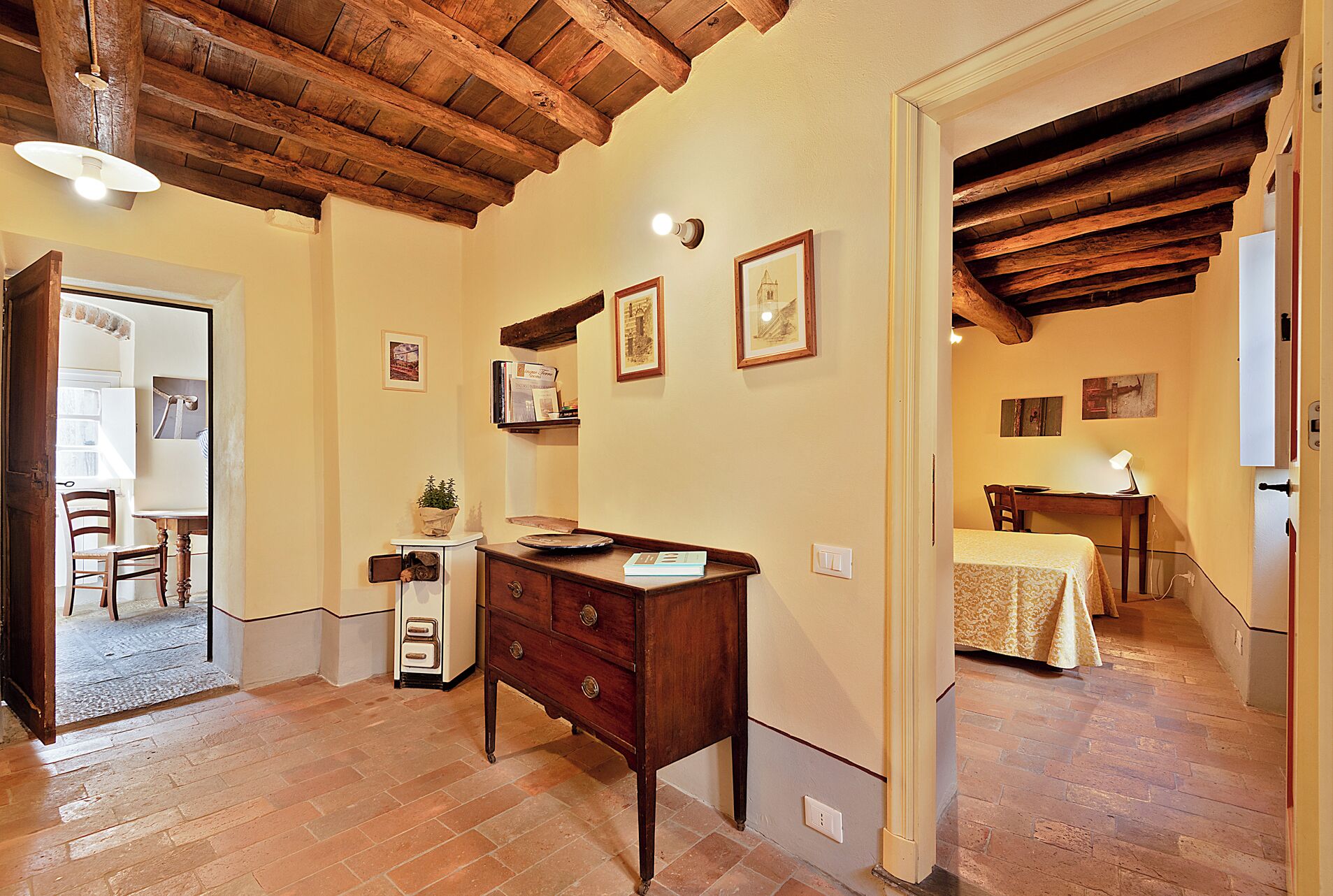 Una habitación con techo de madera, un escritorio con lámpara, una cama con colcha estampada y un aparador con cajones.