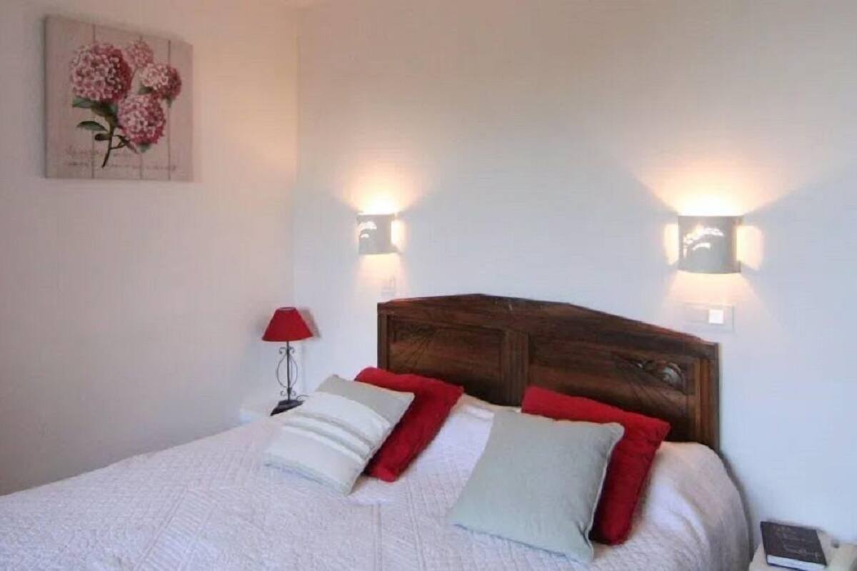 A neatly made bed with white bedding and red and grey pillows, a wooden headboard, and two wall-mounted reading lights.