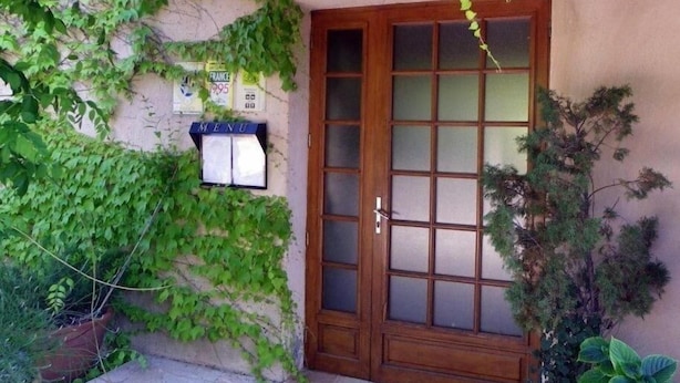Una puerta de madera con un panel de vidrio, una pérgola de madera y una pared con un letrero de menú.