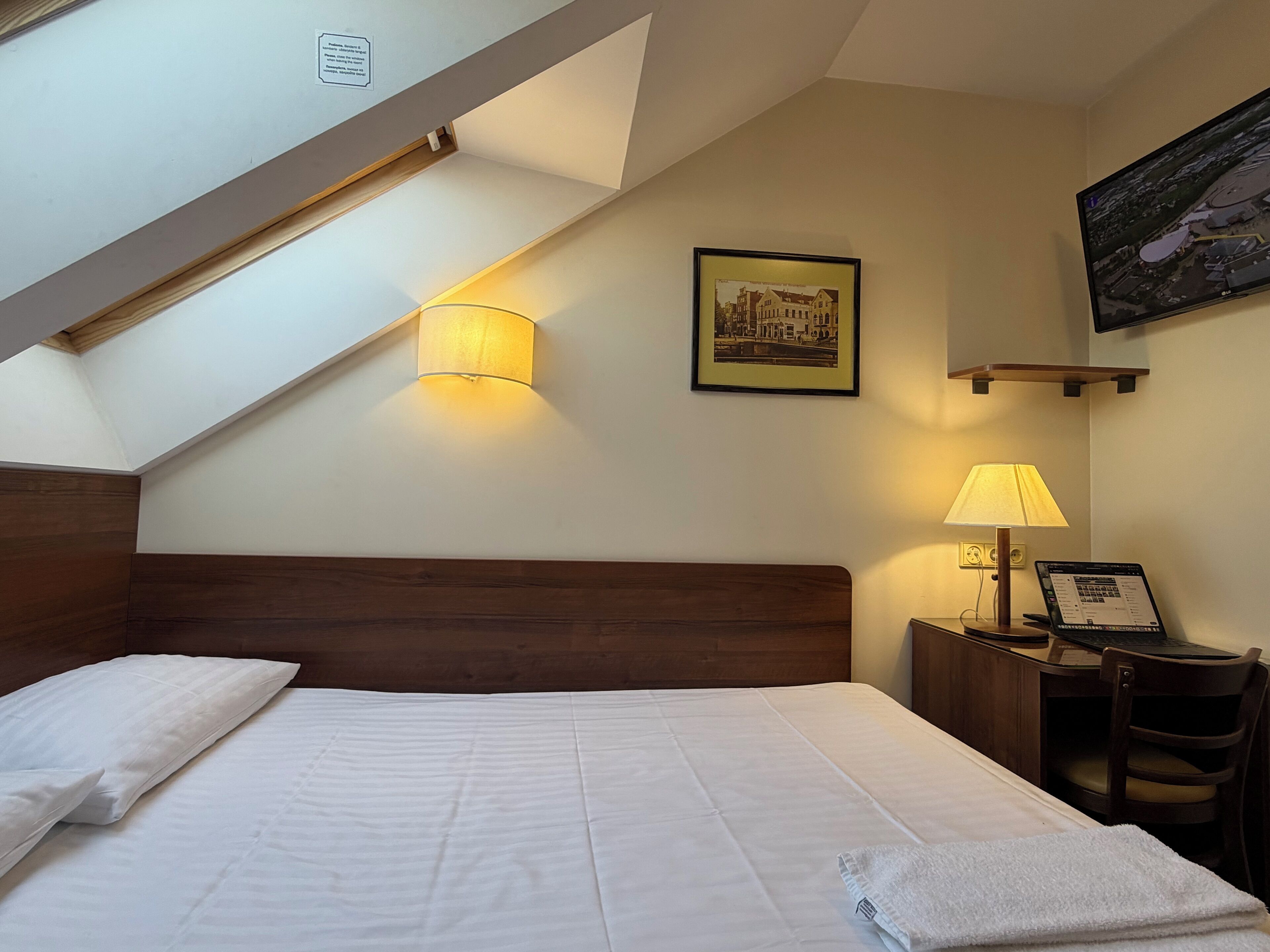 A hotel room with a large bed, a desk with a computer, a lamp, and a painting on the wall.