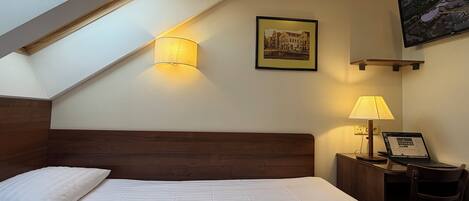 A hotel room with a large bed, a desk with a computer, a lamp, and a painting on the wall.