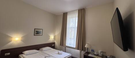 A hotel room with two beds, a desk, a chair, a flat-screen TV, a window with curtains, and a picture on the wall.