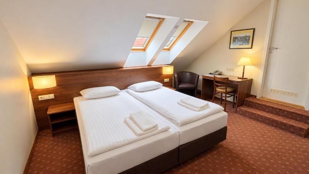 A hotel room with a bed, a desk, a chair, and a small staircase.