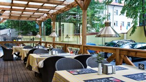 Un espace de restauration en plein air avec des tables en bois et des chaises en osier, abrité par une pergola en bois dotée de panneaux de verre.