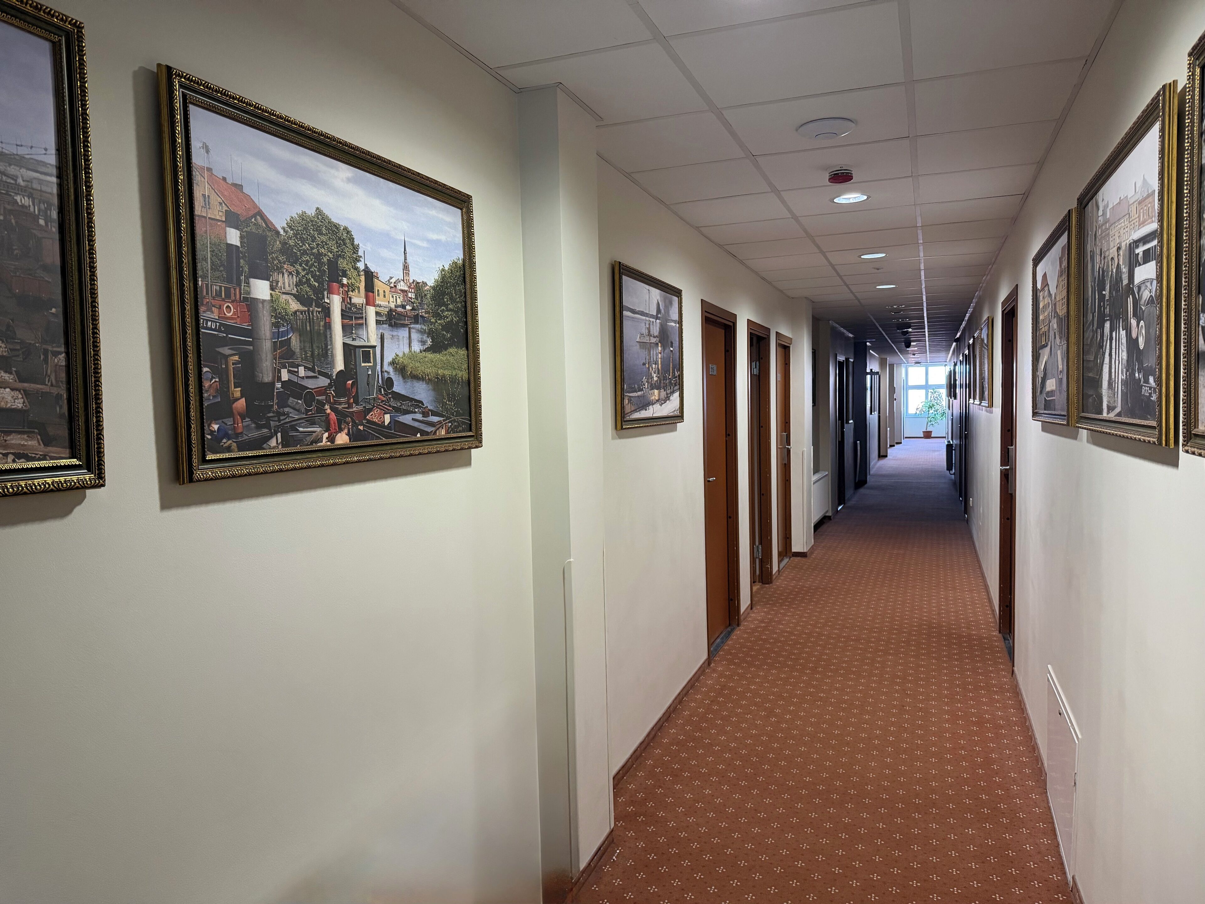 A hallway with framed pictures on the walls, a patterned carpet, and doors leading to rooms.