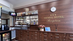 Un espace d’accueil avec un comptoir de réception en bois, une horloge et un panneau indiquant la réception de l’hôtel Memel.