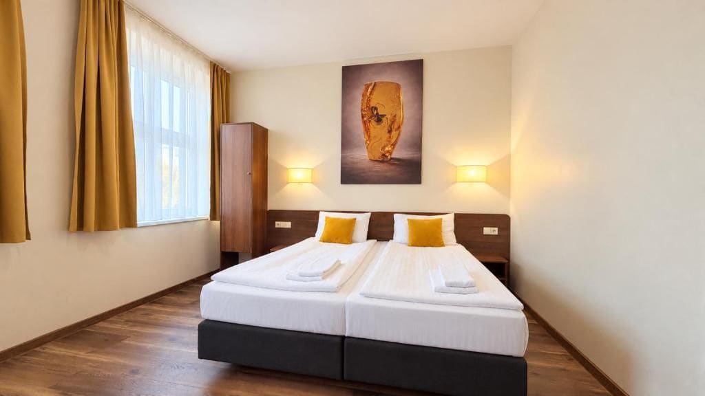Habitación de hotel con cama doble, dos mesitas de noche, un armario y un gran ventanal con cortinas.