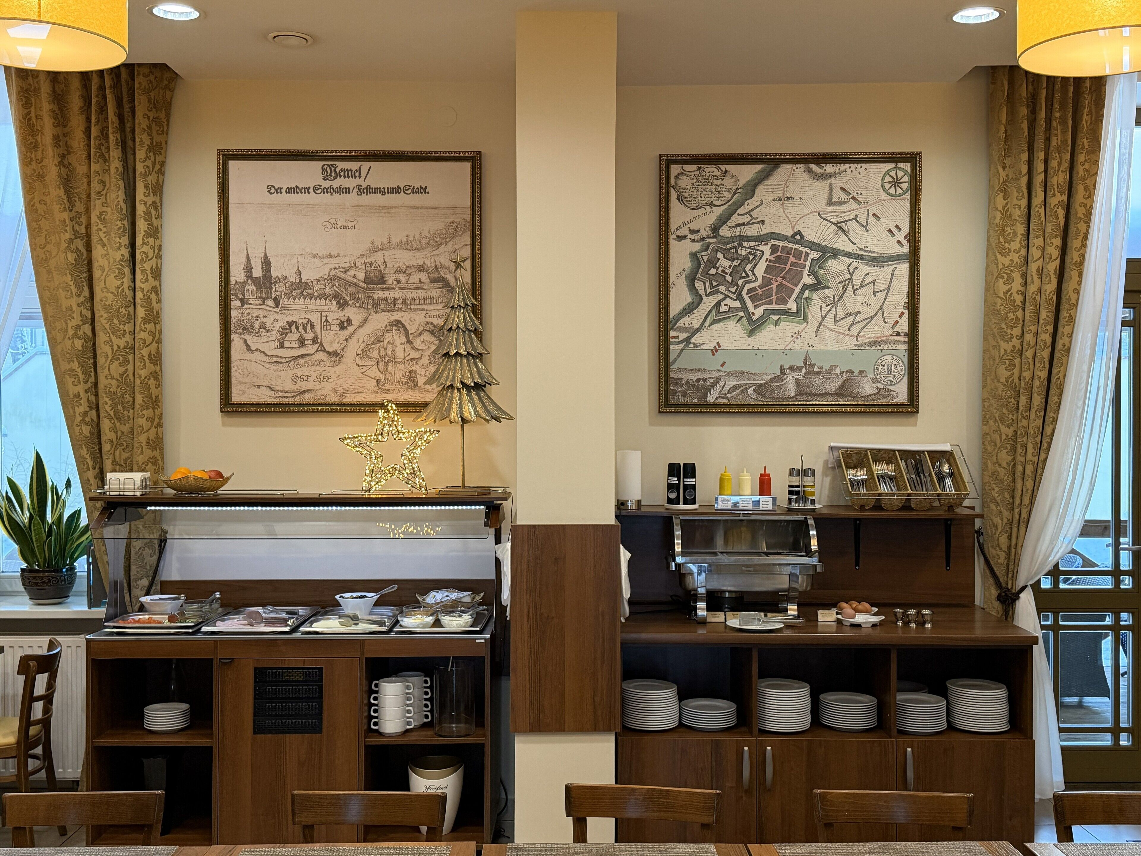 A dining area with a piano, a buffet setup, and two framed maps on the wall.