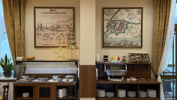 A dining area with a piano, a buffet setup, and two framed maps on the wall.