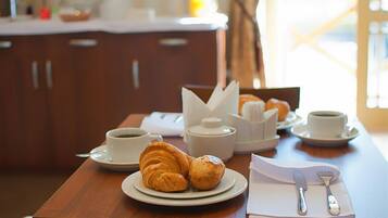 Desayuno con croissants, café y té sobre una mesa de madera.