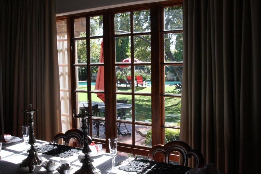 Un comedor con una mesa dispuesta para dos personas, un ventanal con vistas a un jardín y mobiliario exterior.
