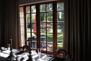 Un comedor con una mesa dispuesta para dos personas, un ventanal con vistas a un jardín y mobiliario exterior.