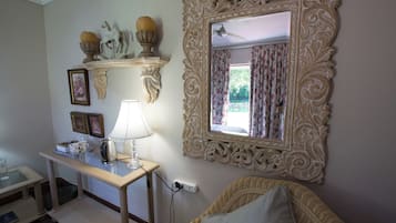 Una habitación con un espejo decorativo, una mesa con lámpara y una silla de mimbre.