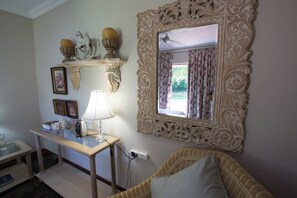 Een kamer met een decoratieve spiegel, een tafel met een lamp en een rieten stoel.