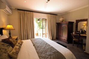 Habitación de hotel con cama, escritorio, silla, armario y un amplio ventanal con cortinas.