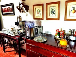 A breakfast bar with coffee machines, tea pots, and a fruit pitcher.