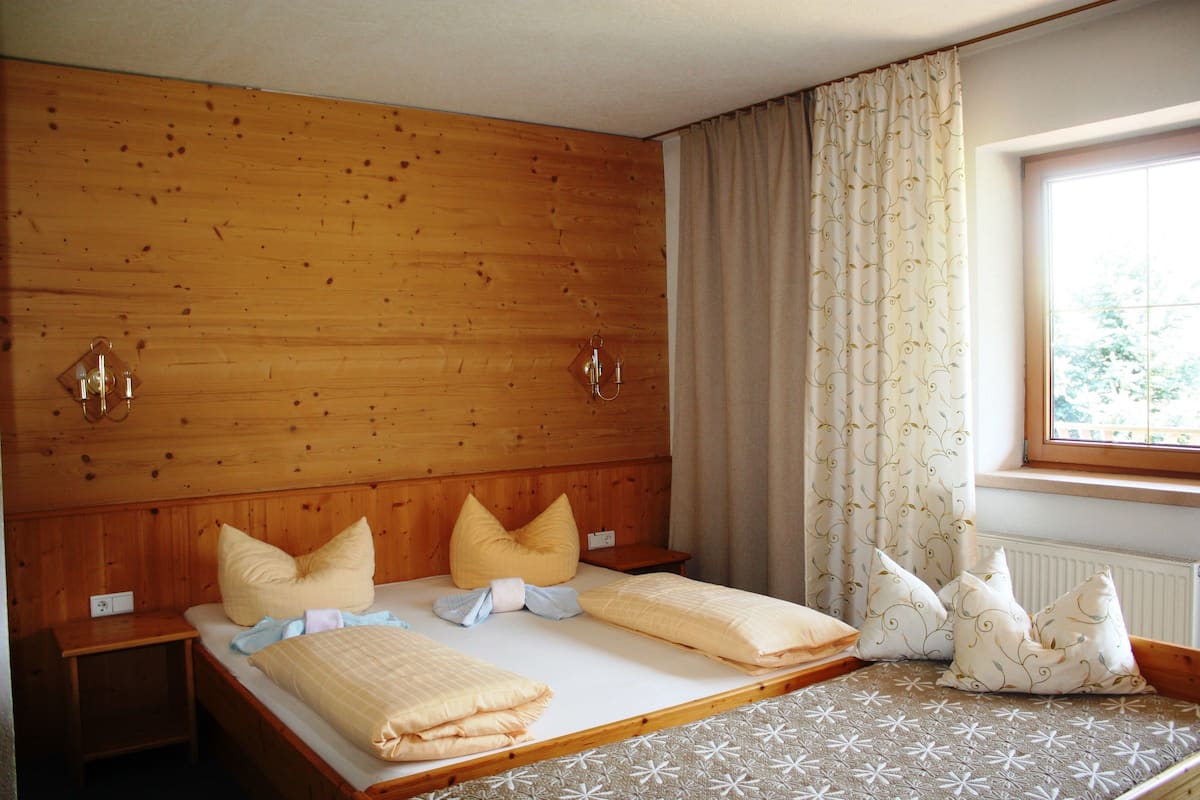 A wooden-paneled room with a bed, two bedside tables, and a window with curtains.