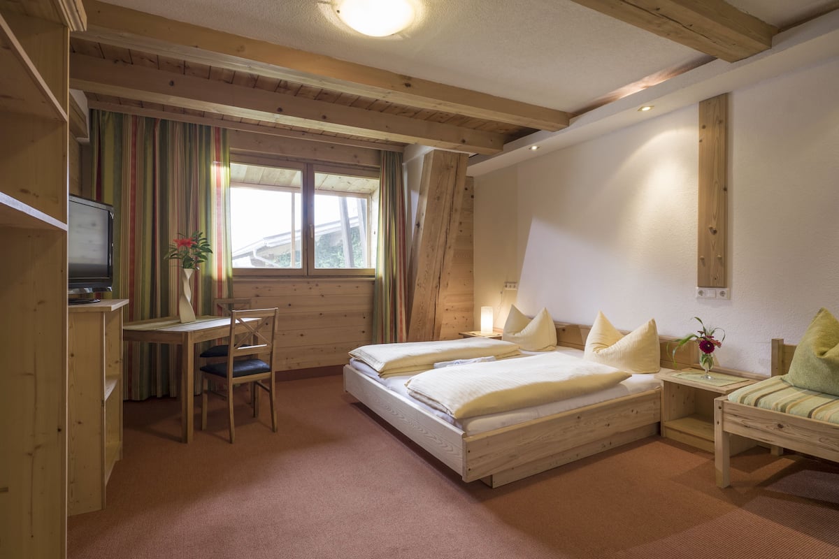 A cozy bedroom with a wooden bed, a desk, and a chair, featuring a window with curtains.