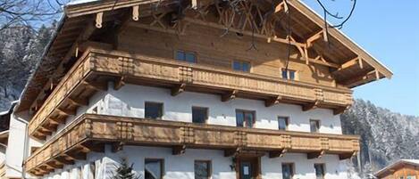 A multi-story wooden building with balconies, a stone staircase, and a snow-covered landscape.