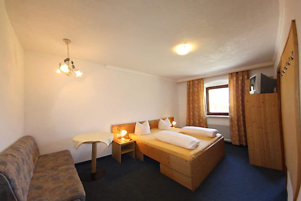A small, cozy room with a single bed, a wooden wardrobe, a small table with a lamp, and a couch.