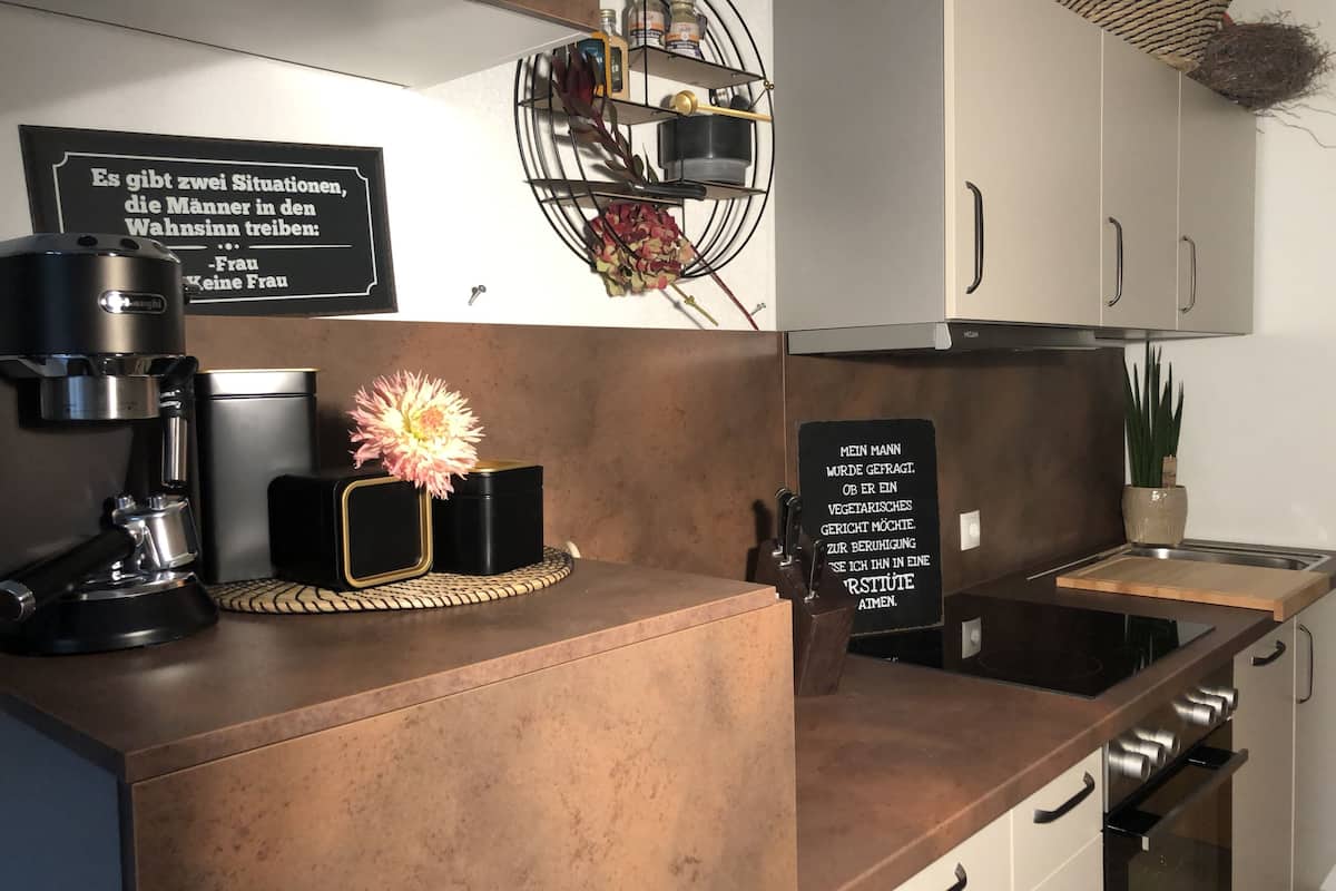 A modern kitchen with a coffee machine, a flower vase, and a sign with a humorous message.