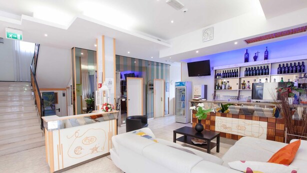 Un'accogliente hall d'hotel in stile moderno, con reception, area salotto e un bar con scaffali pieni di bottiglie.