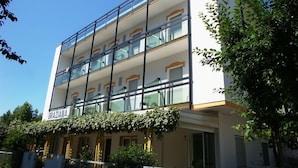 Un edificio moderno a più piani, con balconi dotati di ringhiere in vetro e un cartello all'ingresso con su scritto "GRAZIANA".