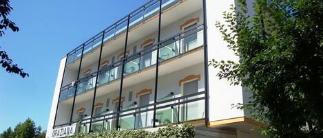 A multi-story building with a modern design, featuring balconies with glass railings and a sign reading "GRAZIANA" at the entrance.