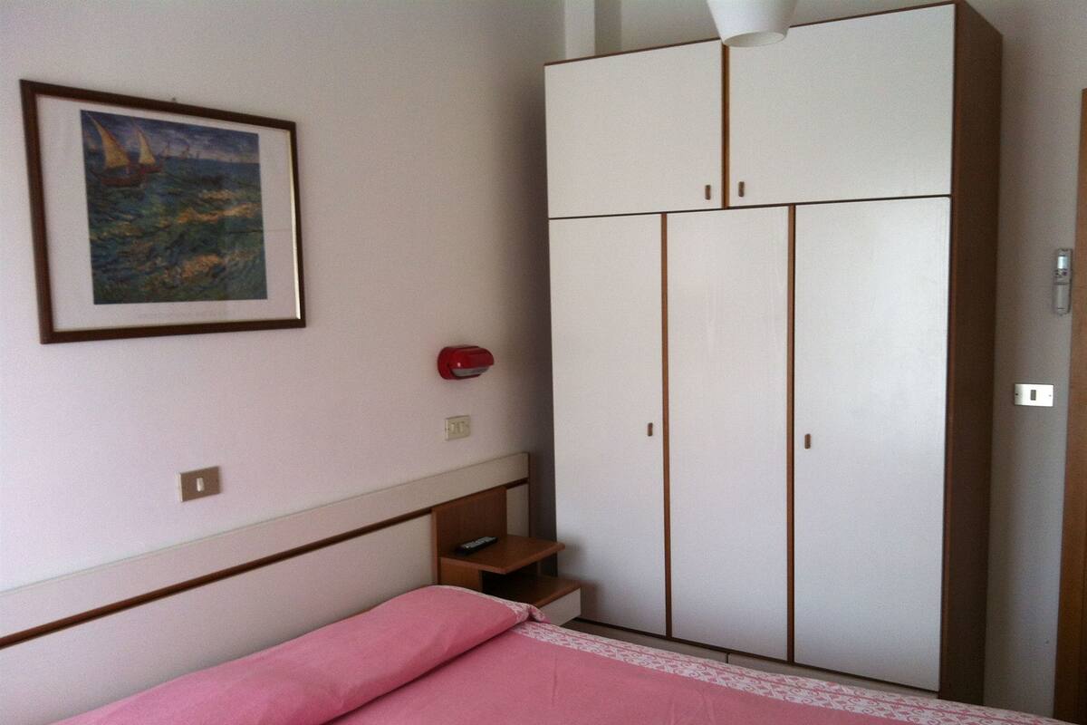 Une chambre à coucher avec un lit, une armoire, un tableau et un objet rouge accroché au mur.