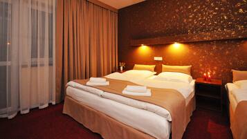 A hotel room with a large bed, a smaller bed, a nightstand with candles, and a large window with curtains.