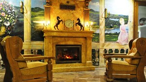 A room with a fireplace, two wooden armchairs, a clock, and a painting of a girl by a lake. - Hotel Karino Spa (Solina)