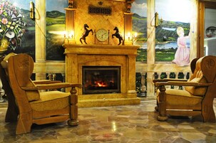 A room with a fireplace, two wooden armchairs, a clock, and a painting of a girl by a lake.