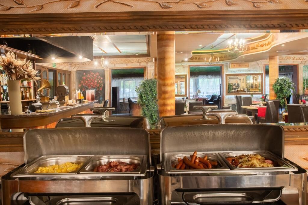 Zona de bufé con varias estaciones de servicio de alimentos, área de bar con barra y taburetes, y espacio de estar con mesas y sillas.