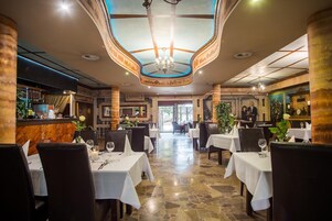 Un restaurante con un espacio central abierto, mesas con manteles blancos y una araña.
