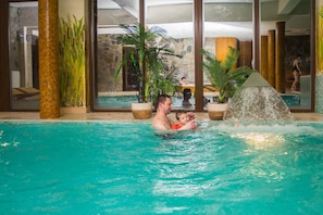 An indoor swimming pool with clear water, surrounded by large windows and tropical plants. - Hotel Karino Spa (Solina)