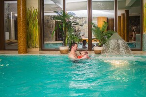 Una piscina interior con agua cristalina, rodeada de grandes ventanales y plantas tropicales.