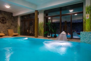 Una piscina interior con fuente, sillones de madera y ventanas amplias.
