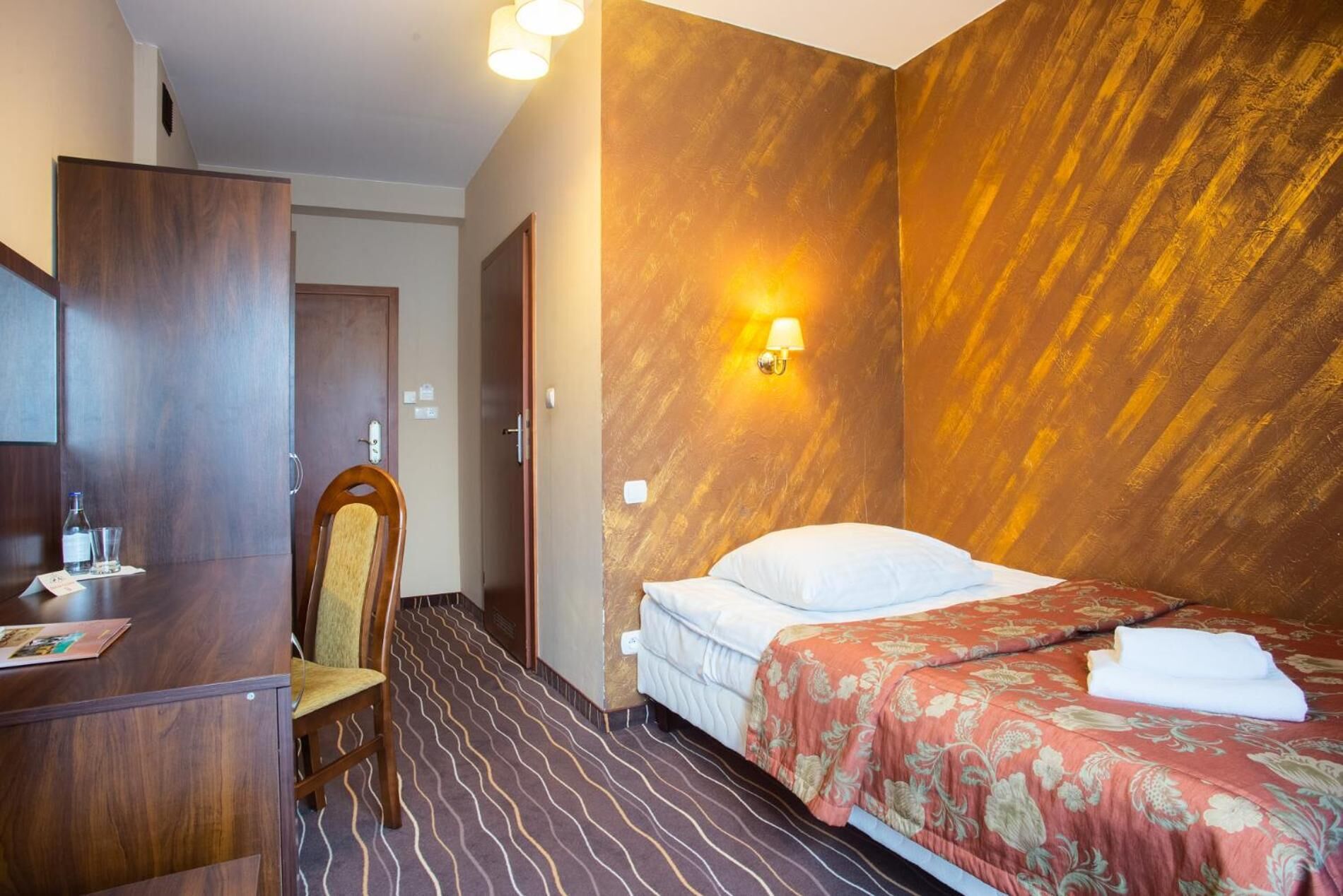 Ein Hotelzimmer mit Bett, Schreibtisch, Stuhl und Wandlampe.