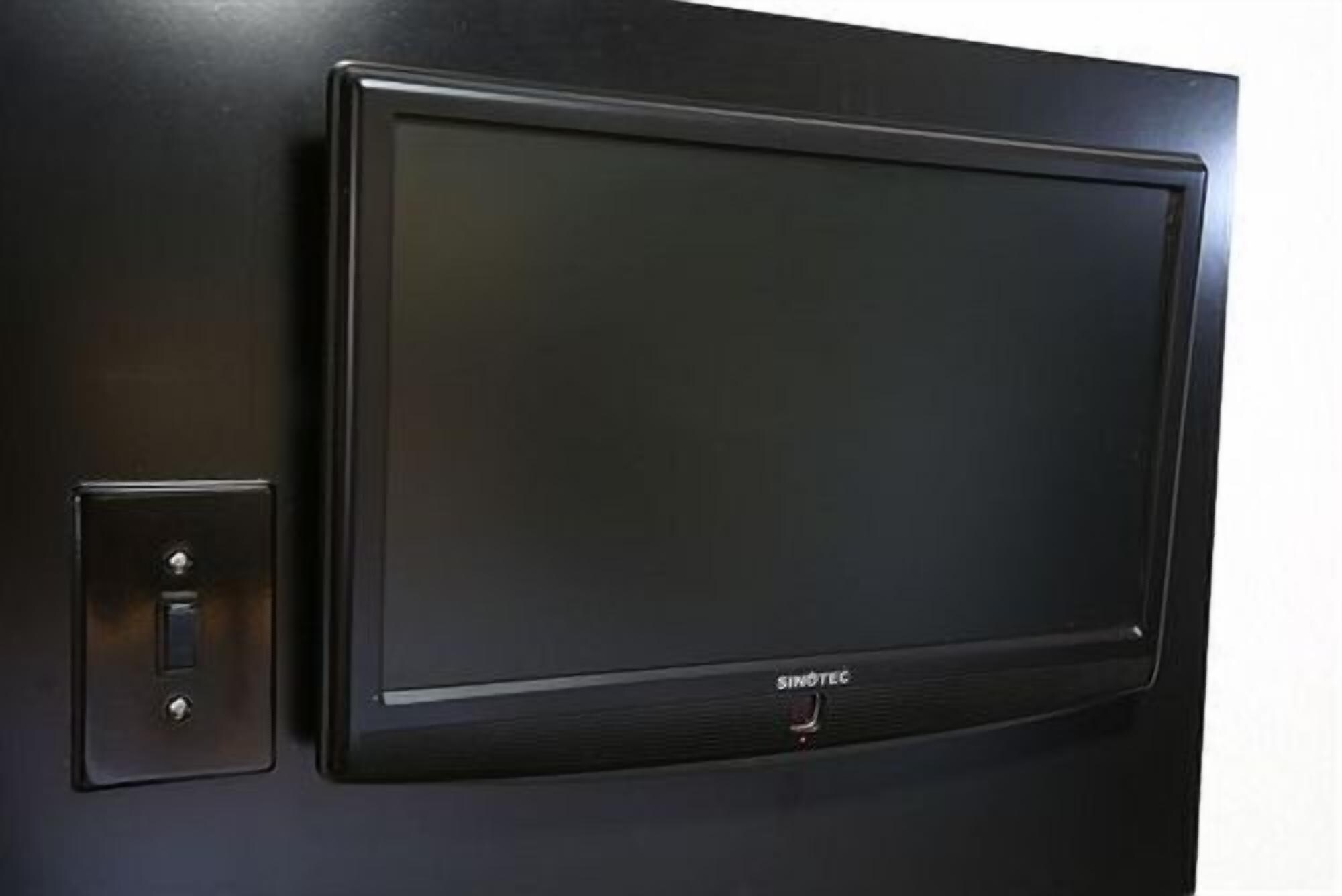 Musta seinälle asennettu televisio, jonka vasemmalla puolella on kaukosäädin.