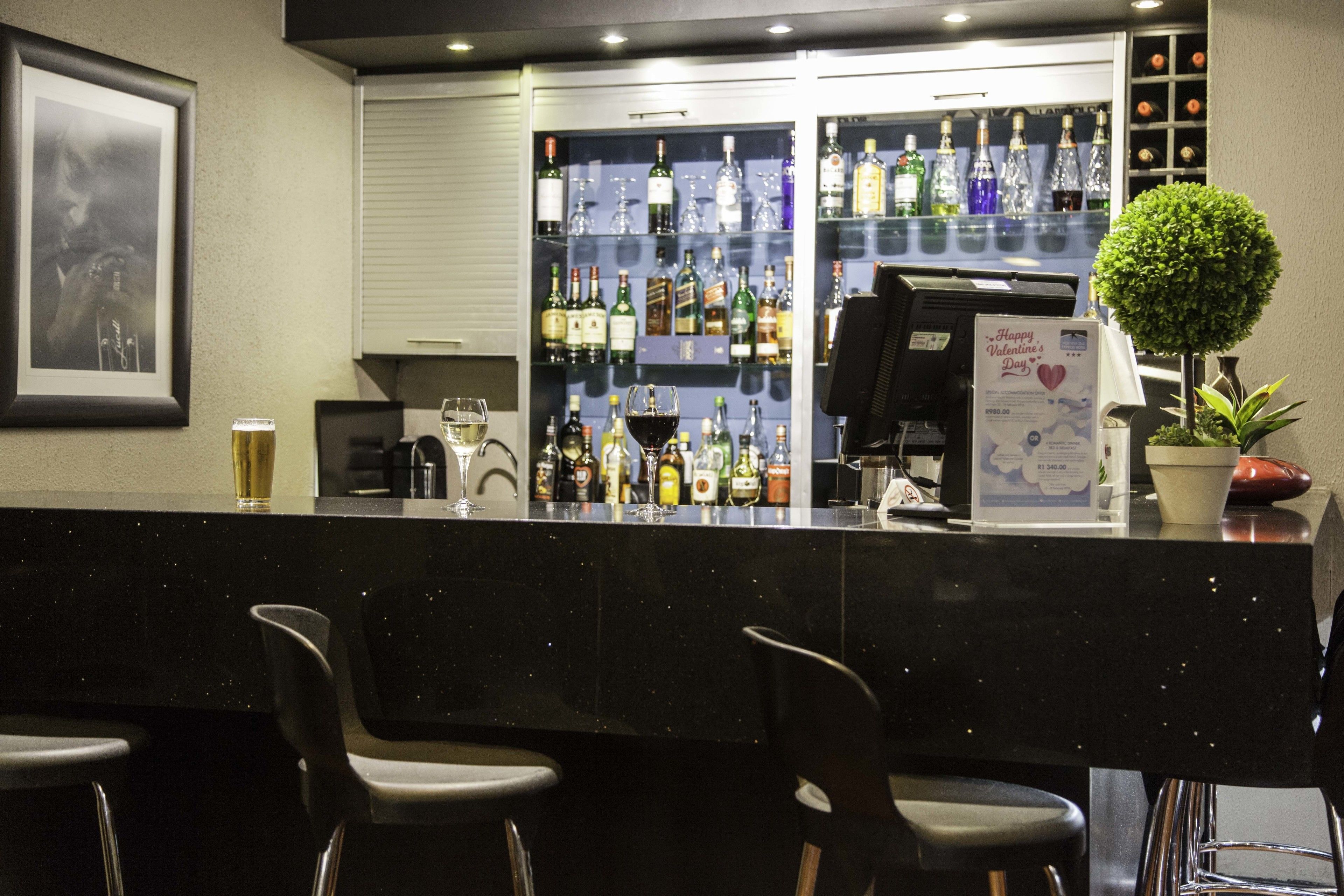 A bar area with a counter, shelves of liquor bottles, a framed picture on the wall, and a potted plant.