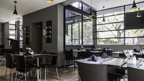 Un restaurante moderno con mobiliario negro, ventanas amplias e iluminación colgante.