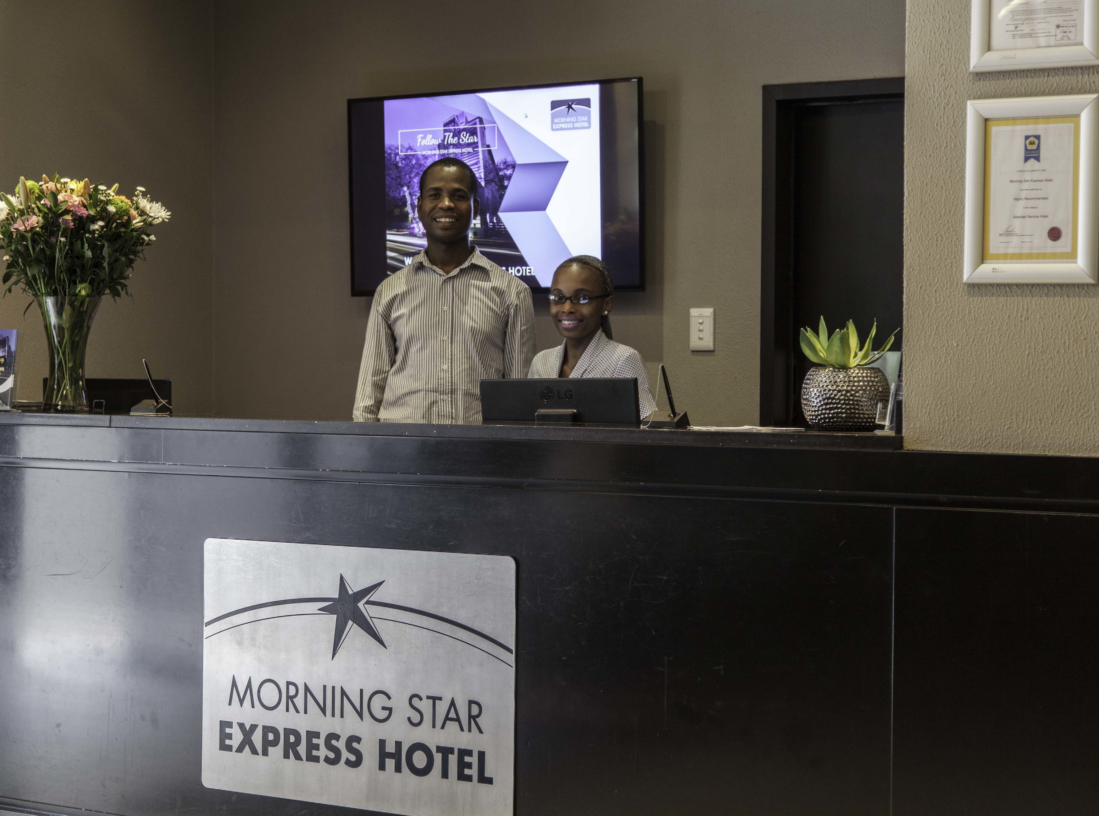 Un mostrador de recepción en el Hotel Morning Star Express, con una pantalla de televisión mostrando una imagen promocional.