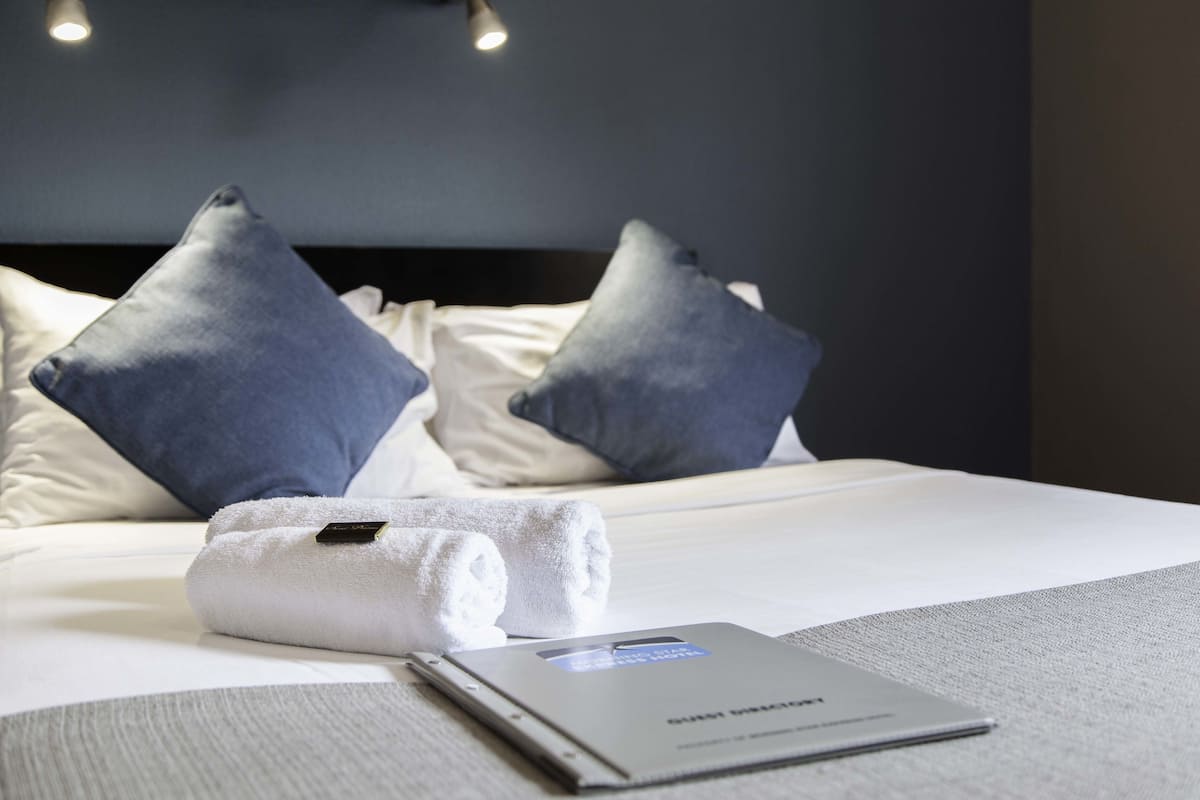 A neatly made bed with a folded white towel and a book on the bed.