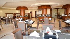 Un amplio comedor de hotel con varias mesas y sillas, pilares de madera maciza y una decoración interior moderna.