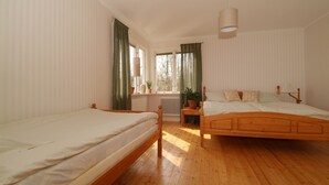 Un dormitorio con dos camas de madera, una ventana con cortinas, un radiador y una lámpara colgante.