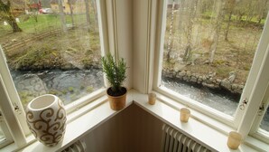 Una ventana con vistas a un paisaje rural, una planta en maceta y un jarrón decorativo.
