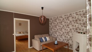 Una sala de estar con un sofá, una mesa de centro de madera, una lámpara colgante, un papel tapiz estampado y una chimenea.