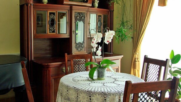 Un coin repas avec une table ronde recouverte d’une nappe en dentelle, entourée de chaises en bois.